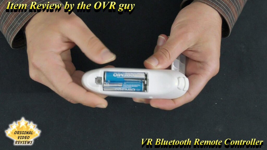 Close-up of the VR Bluetooth Remote Controller held by The OVR Guy, showing the bottom battery compartment with two small batteries (AAA size).