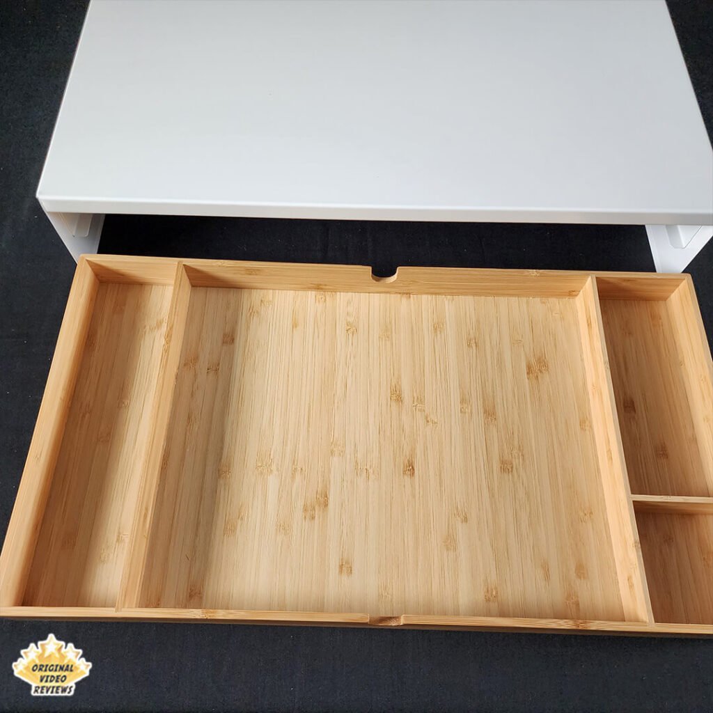 Close-up top view of the IKEA ELLOVEN Monitor Stand with the bamboo drawer fully extended, showing its fixed compartments.