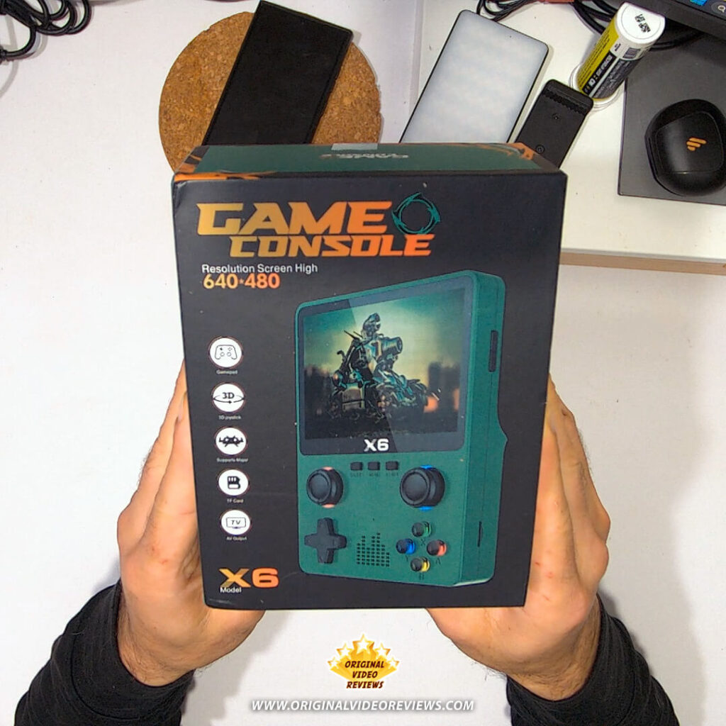 Hands holding the X6 handheld retro game console retail box, showing the device image and features.