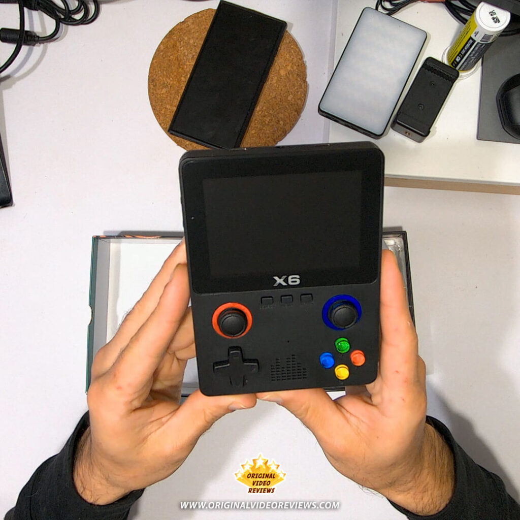 Front view of the X6 handheld retro gaming console being held in both hands, screen turned off.