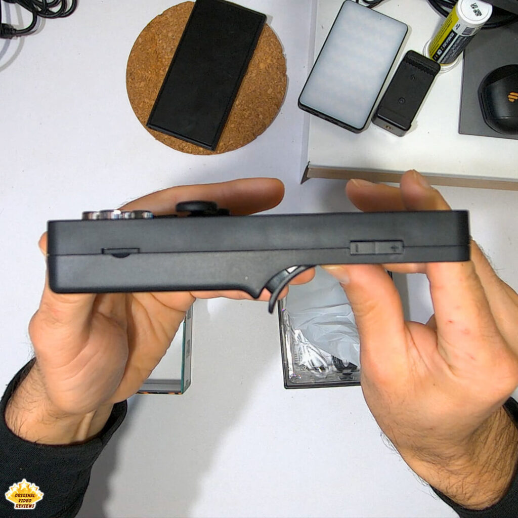 Hands holding the X6 handheld gaming console, showing side view with volume buttons, trigger grip, and microSD slot