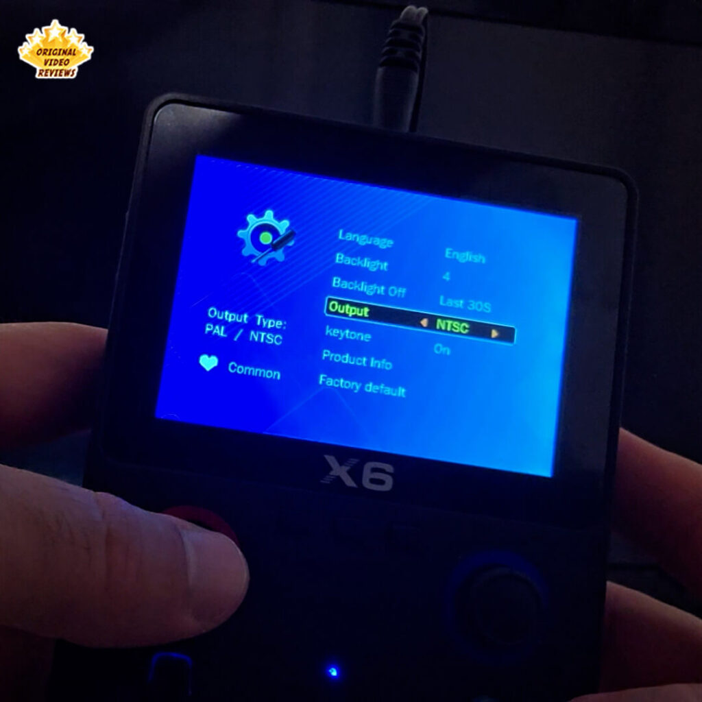 X6 handheld console displaying the settings menu with output type set to NTSC, showing options like language, backlight, and factory reset.