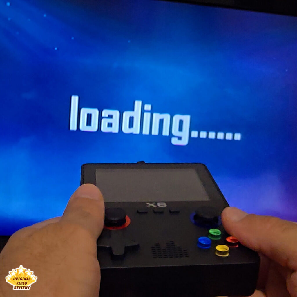 Hands holding the X6 handheld console connected to a TV, showing a "loading..." screen.