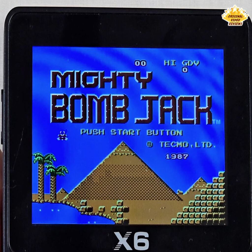 Title screen of Mighty Bomb Jack displayed on the X6 handheld console, showing pyramids and palm trees in the background.