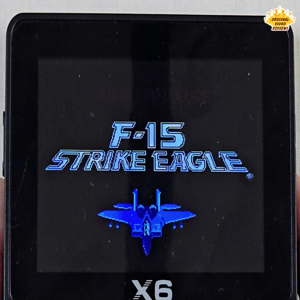 Title screen of F-15 Strike Eagle displayed on the X6 handheld console, featuring a blue fighter jet graphic.