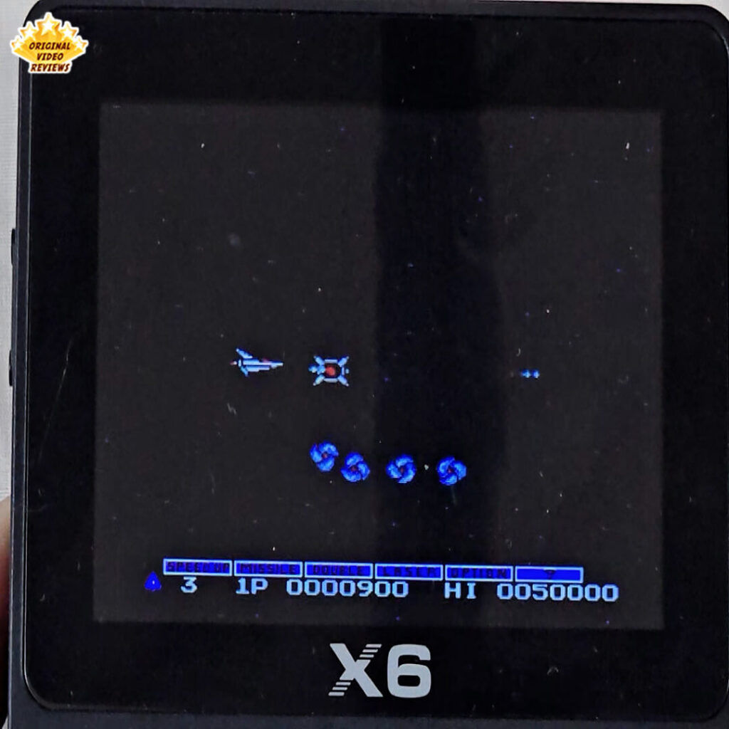 Gameplay of Gradius on the X6 handheld console showing the spaceship Vic Viper shooting enemies in space.