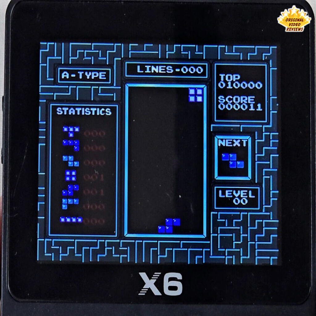 X6 handheld console displaying the classic puzzle game Tetris with falling blue blocks.