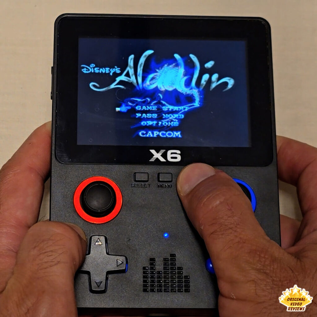 Close-up of the X6 handheld console displaying the title screen of Disney's Aladdin by Capcom.
