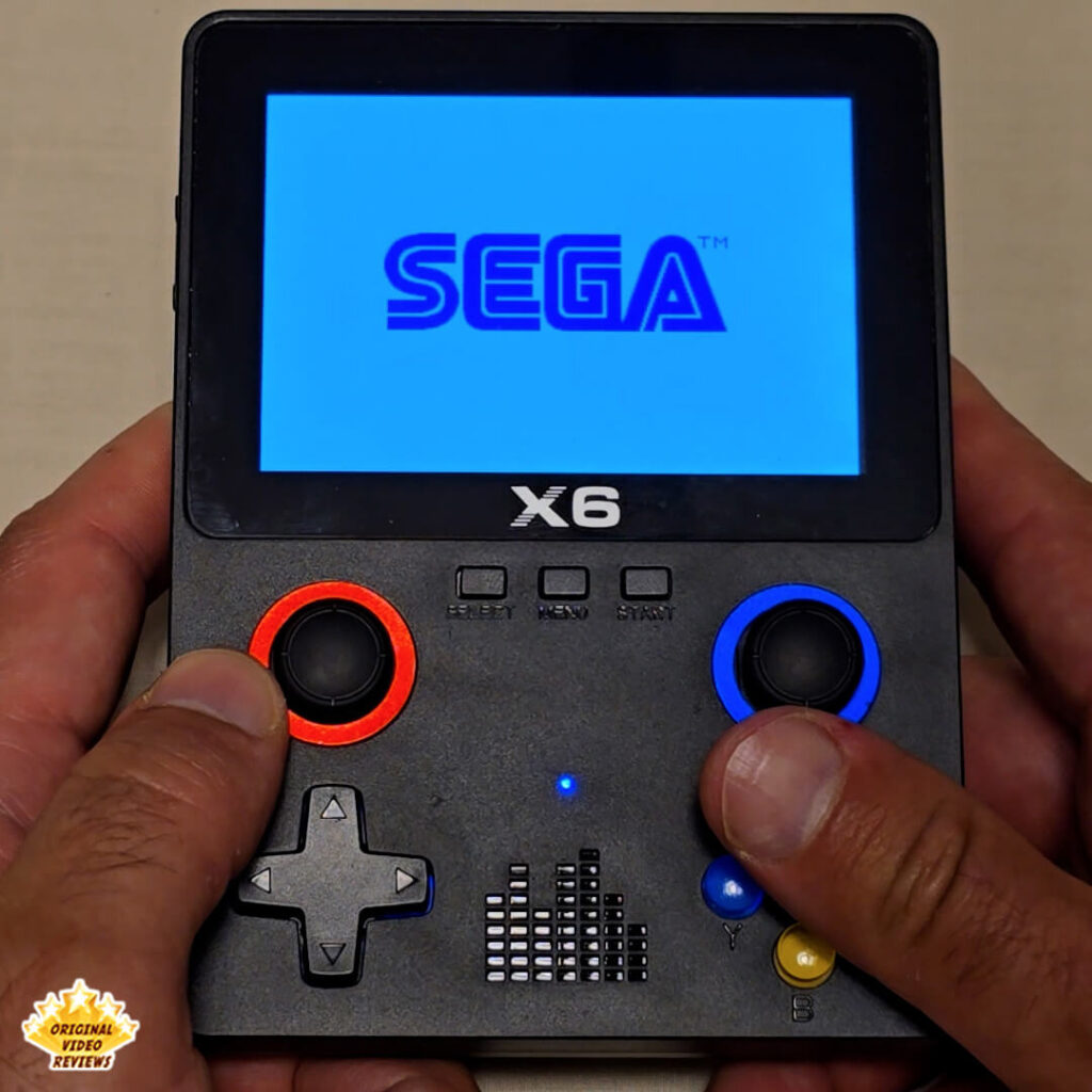Close-up of the X6 handheld console displaying the blue SEGA logo on its screen.