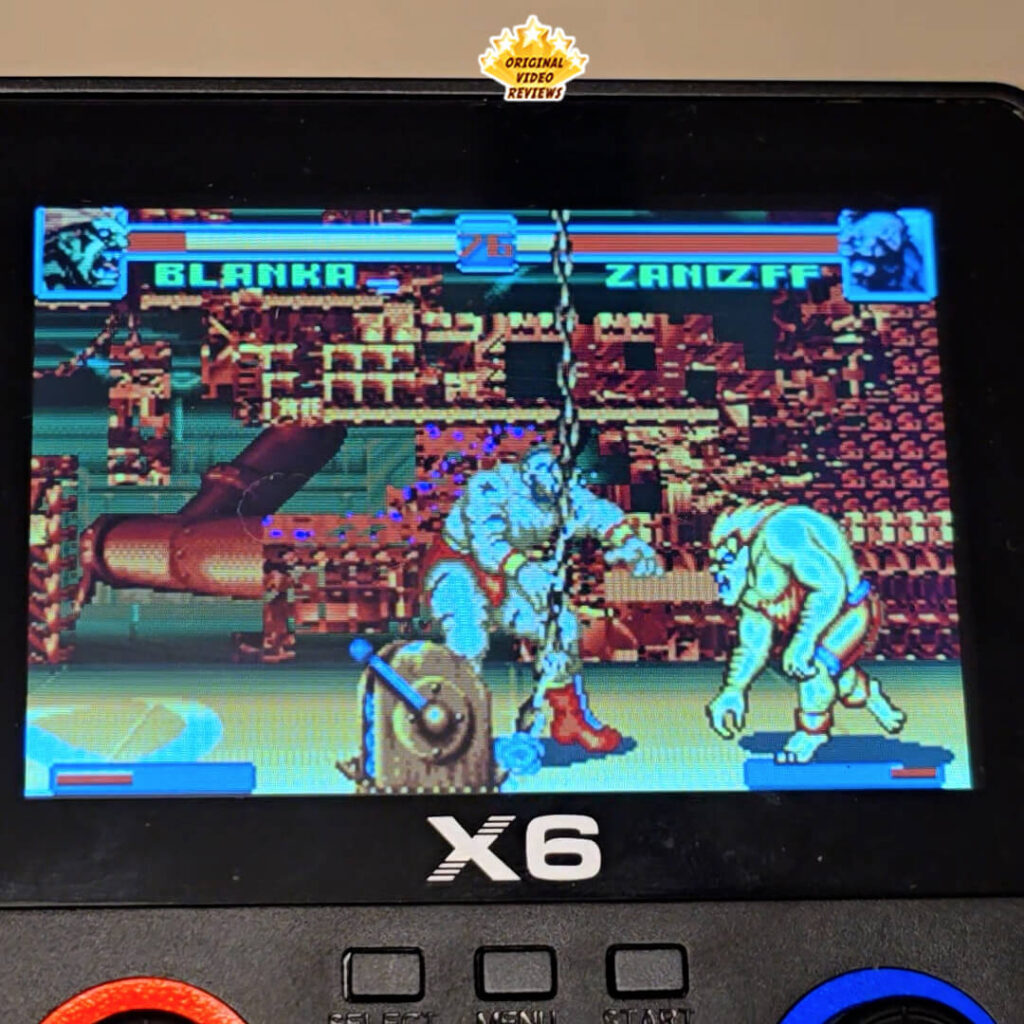 Close-up of the X6 handheld gaming console screen showing a fight between Blanka and Zangief in a classic arcade-style game.