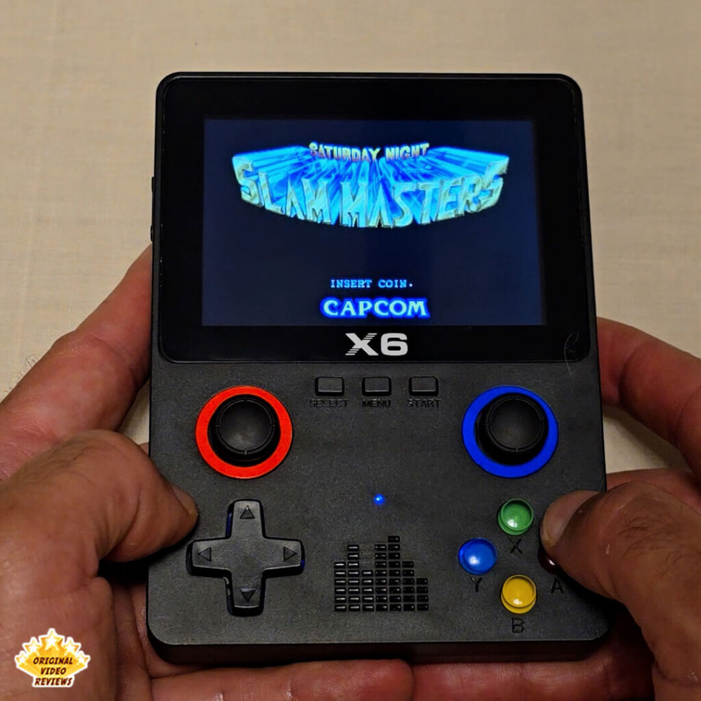Close-up of the X6 handheld retro gaming console displaying the title screen of "Strider". The console's buttons and joysticks are clearly visible.