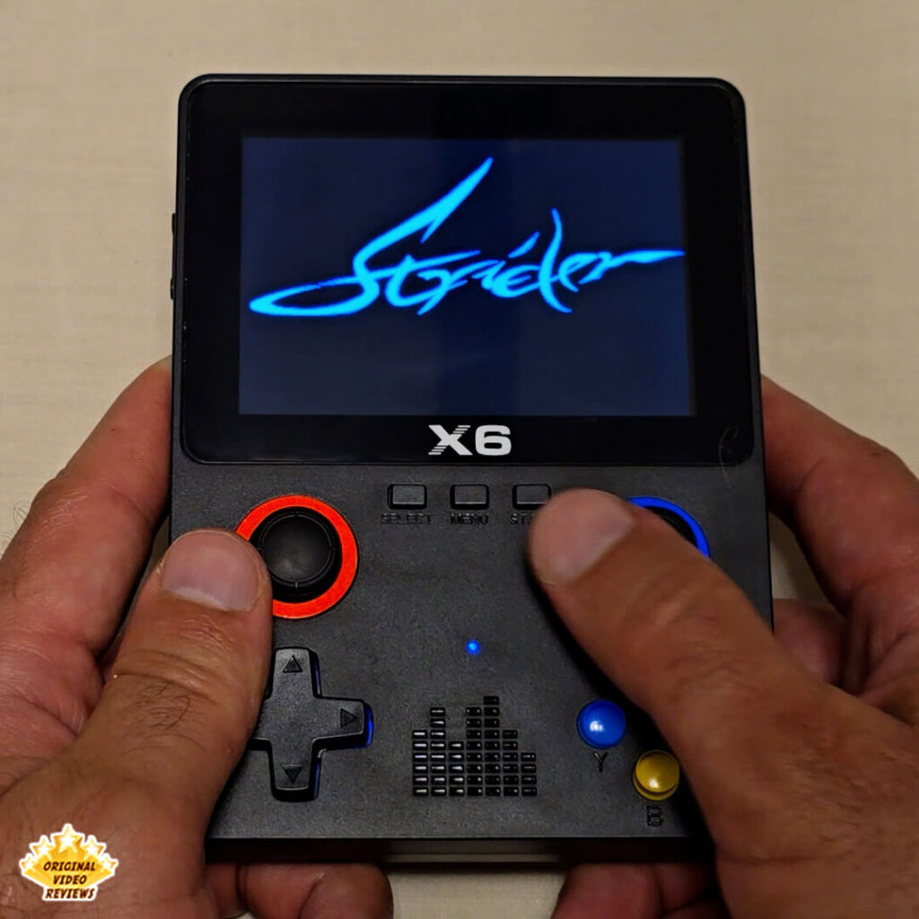 Close-up of the X6 handheld retro gaming console displaying the title screen of "Strider". The console's buttons and joysticks are clearly visible.