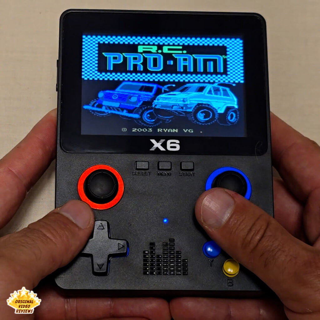 Close-up of the X6 handheld retro gaming console displaying the title screen of "R.C. Pro-Am". The console's buttons and joysticks are clearly visible.