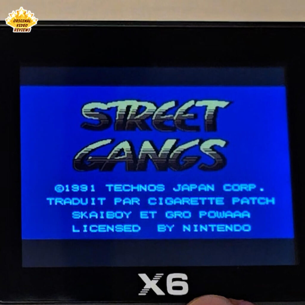 Close-up of the X6 handheld retro gaming console displaying the title screen of "Street Gangs". The console's logo and partial controls are visible at the bottom of the frame.
