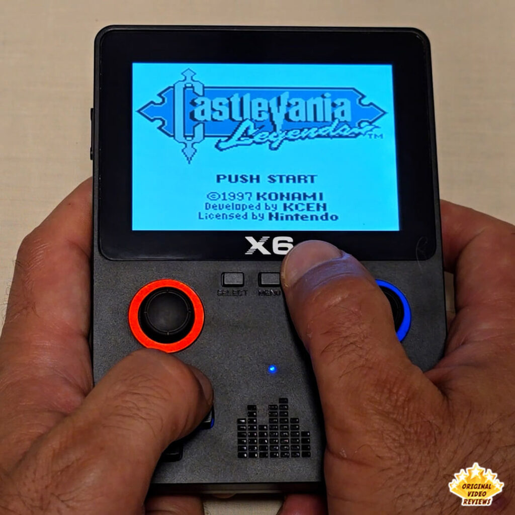 Close-up of the X6 handheld retro gaming console displaying the title screen of Castlevania Legends. The console's buttons and joysticks are clearly visible.