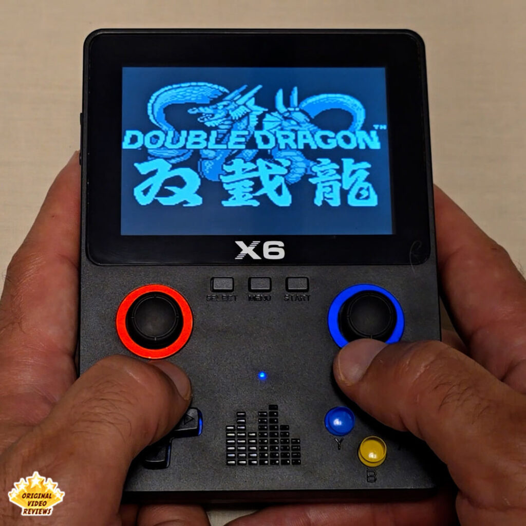 Close-up of the X6 handheld retro gaming console displaying the title screen of Double Dragon. The console's buttons and joysticks are clearly visible.