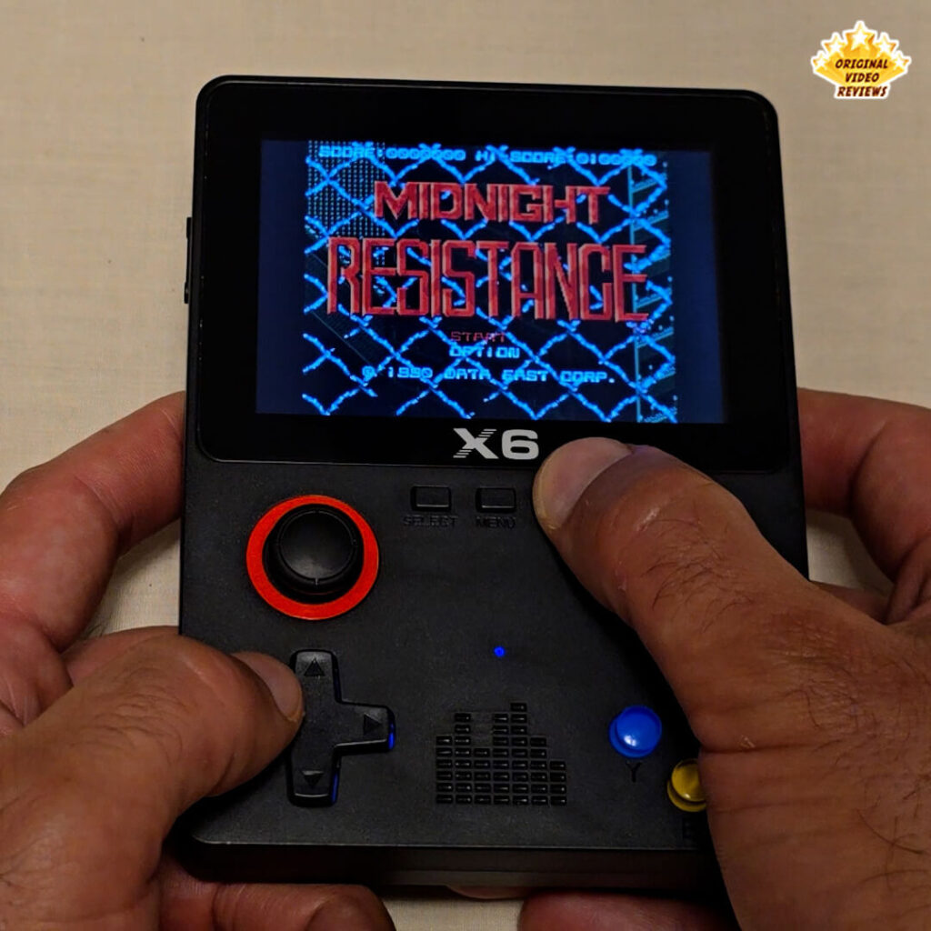 Close-up of the X6 handheld retro gaming console displaying the title screen of "Midnight Resistance," showing the game's logo and options.