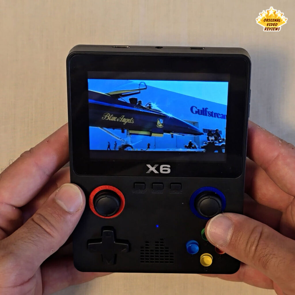 Close-up of the X6 handheld retro gaming console playing a video featuring a Blue Angels jet with Gulfstream branding.