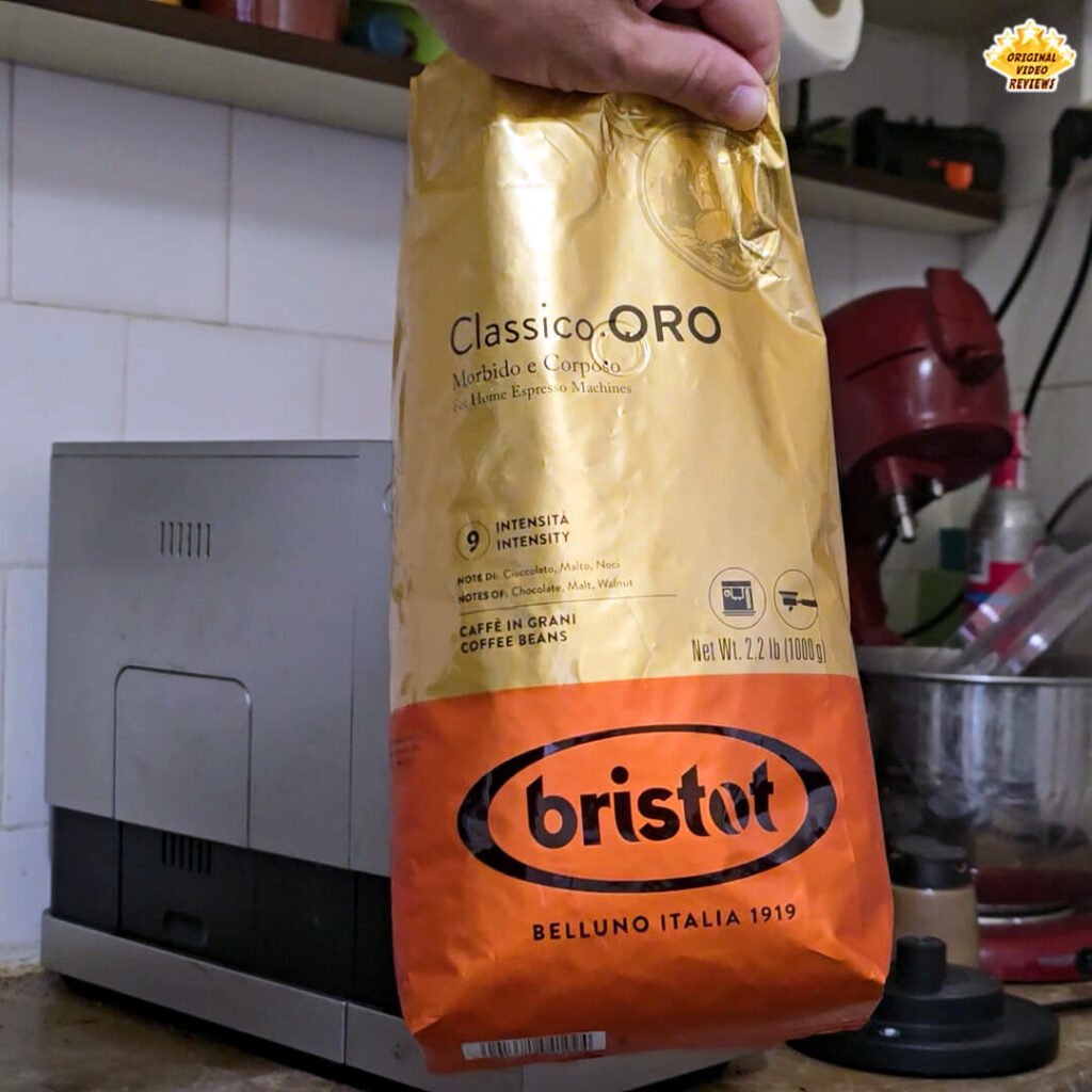 The OVR Guy holding an open bag of Bristot Classico Oro coffee beans in front of a BEANS fully automatic espresso machine, moments before brewing the first cup.