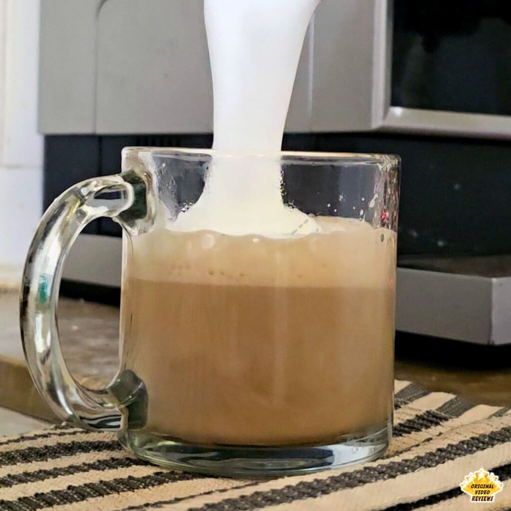 The OVR Guy pouring frothed milk into a glass mug of Bristot Classico Oro coffee, creating a rich layer of foam. The image captures the authentic, home-style preparation moment from the review.