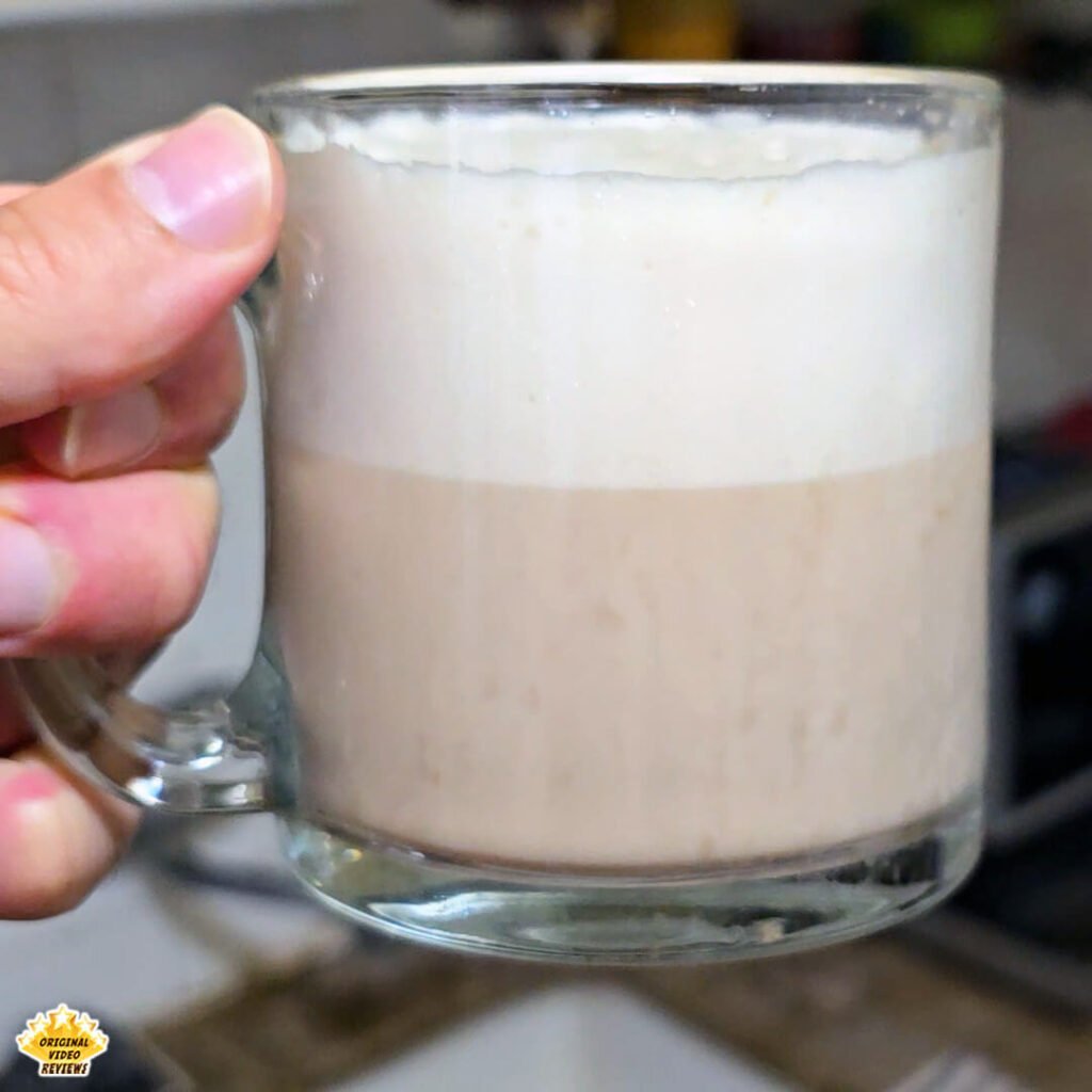 The OVR Guy holding a glass mug filled with Bristot Classico Oro coffee topped with frothed milk, marking the final step of the first tasting experience featured in the review.