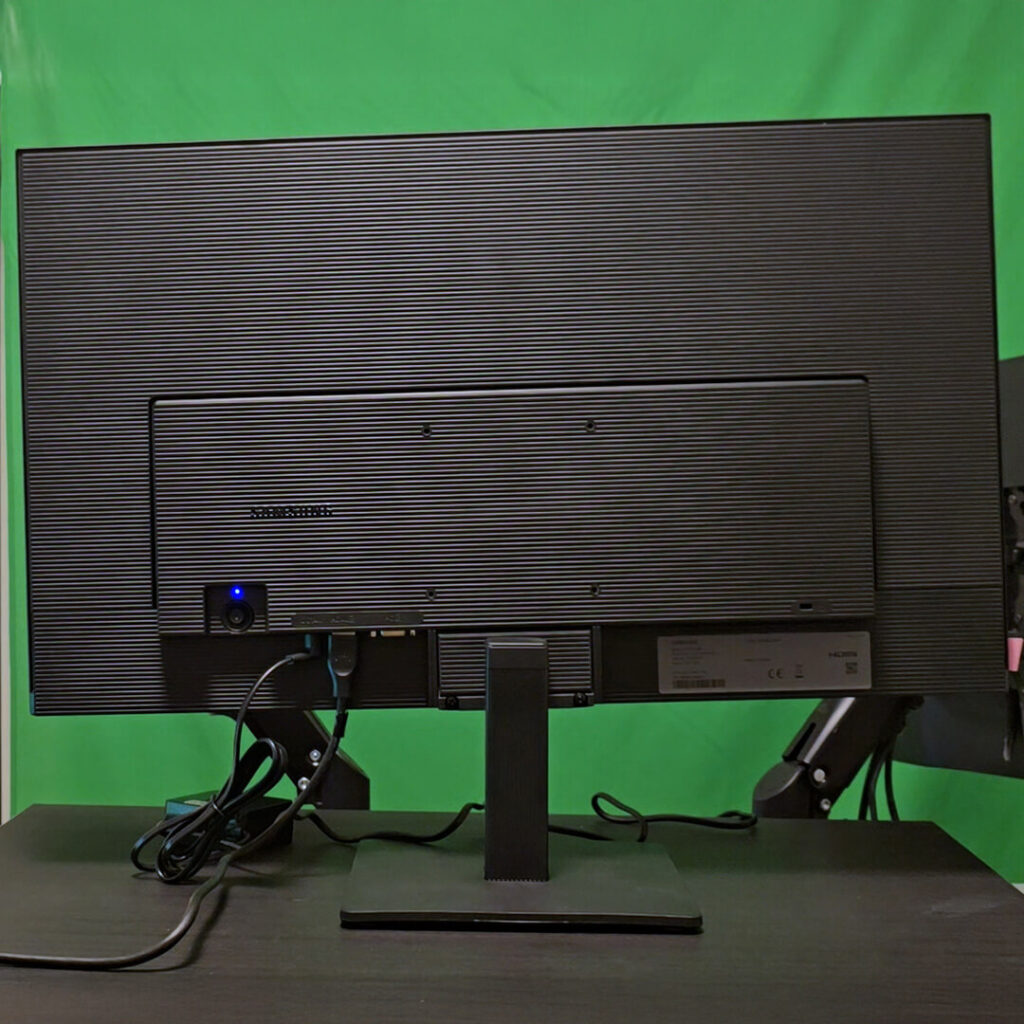 Rear view of the Samsung Essential Monitor S3 fully assembled on its stand with a blue power indicator light active.