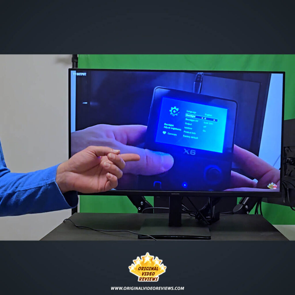 The OVR Guy pointing to a handheld device displayed on the Samsung Essential Monitor S3 during a video review.