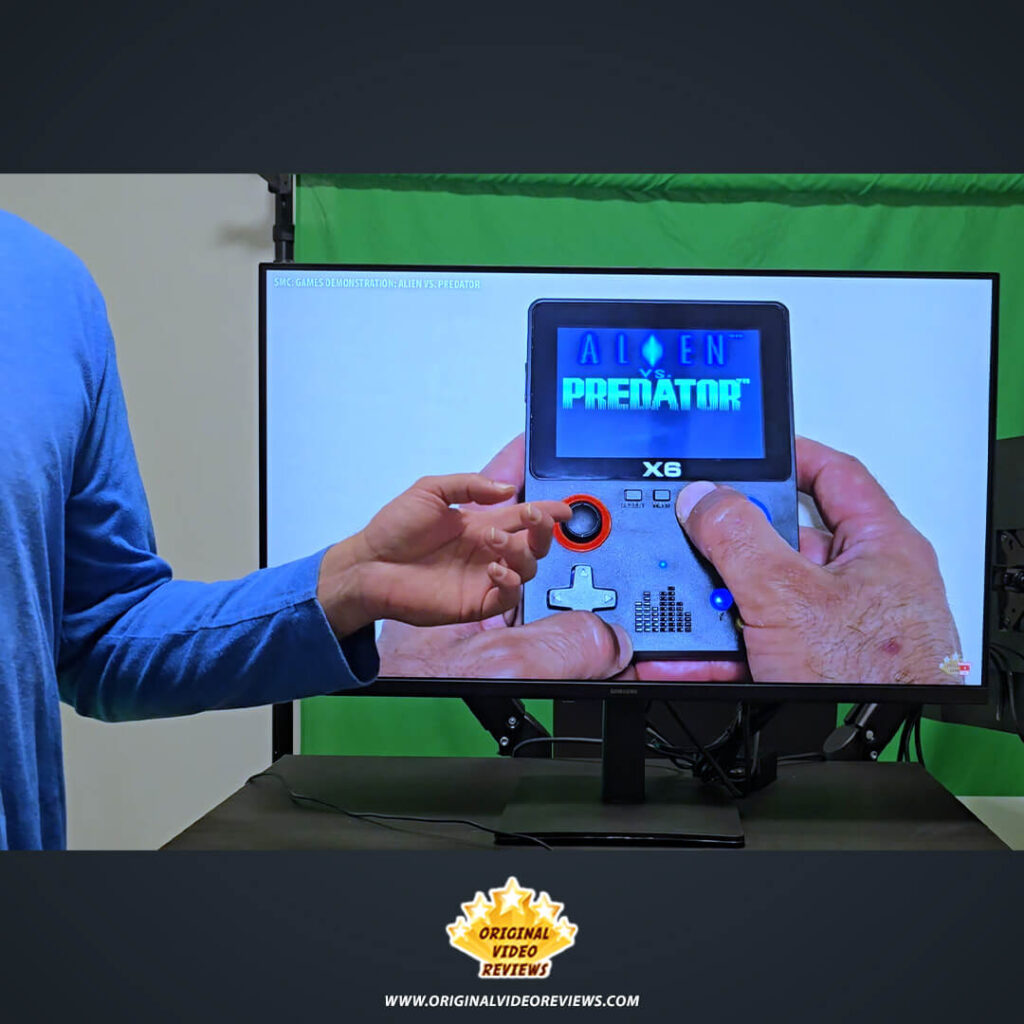 The OVR Guy gesturing toward the Samsung Essential Monitor S3 while it displays a video of a handheld gaming console.