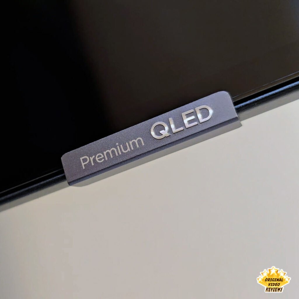 Macro shot of the "Premium QLED" silver branding tag on the bezel of the TCL P89K 65-inch 4K QLED TV, from a review by Original Video Reviews.