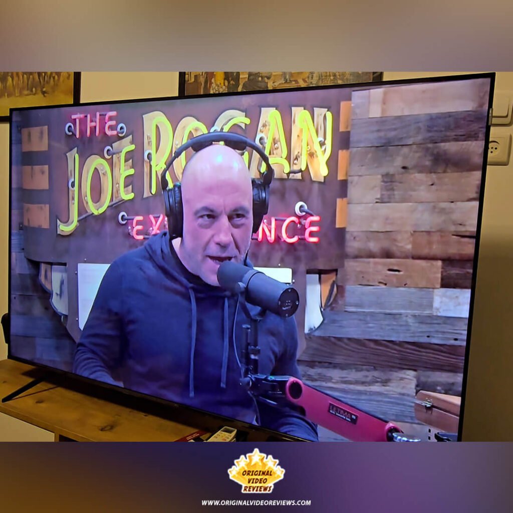 Angled shot of the TCL P89K 65-inch 4K QLED TV playing "The Joe Rogan Experience" on Spotify, demonstrating app activation and media streaming during a review by Original Video Reviews.