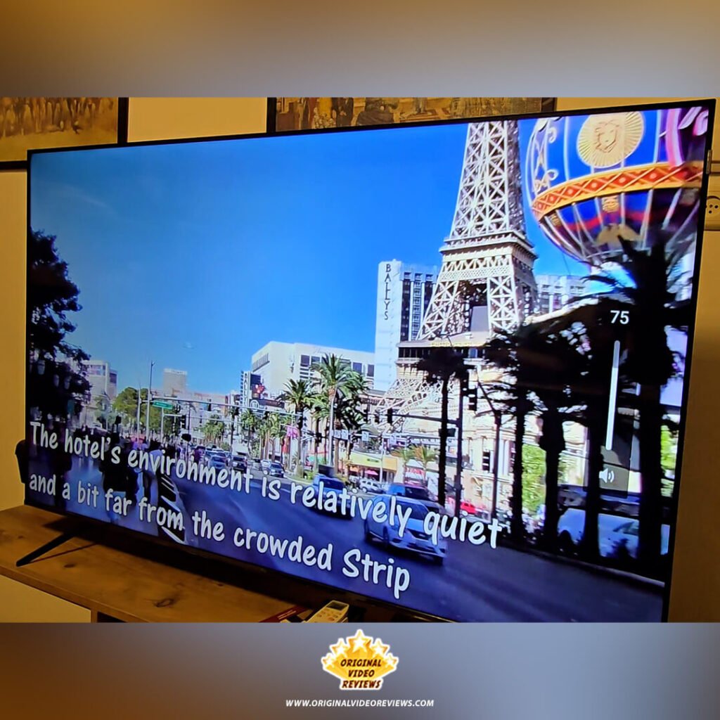 The TCL P89K 65-inch 4K QLED TV screen playing a travel video from the OVR TRAVEL YouTube channel, showing the Las Vegas Strip and Eiffel Tower replica with subtitles, from a review by Original Video Reviews.