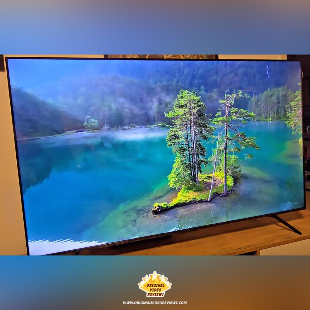 A high-resolution 4K nature video of a small island with pine trees in the center of a turquoise lake, displayed on the TCL P89K 65-inch QLED TV for a review by Original Video Reviews.