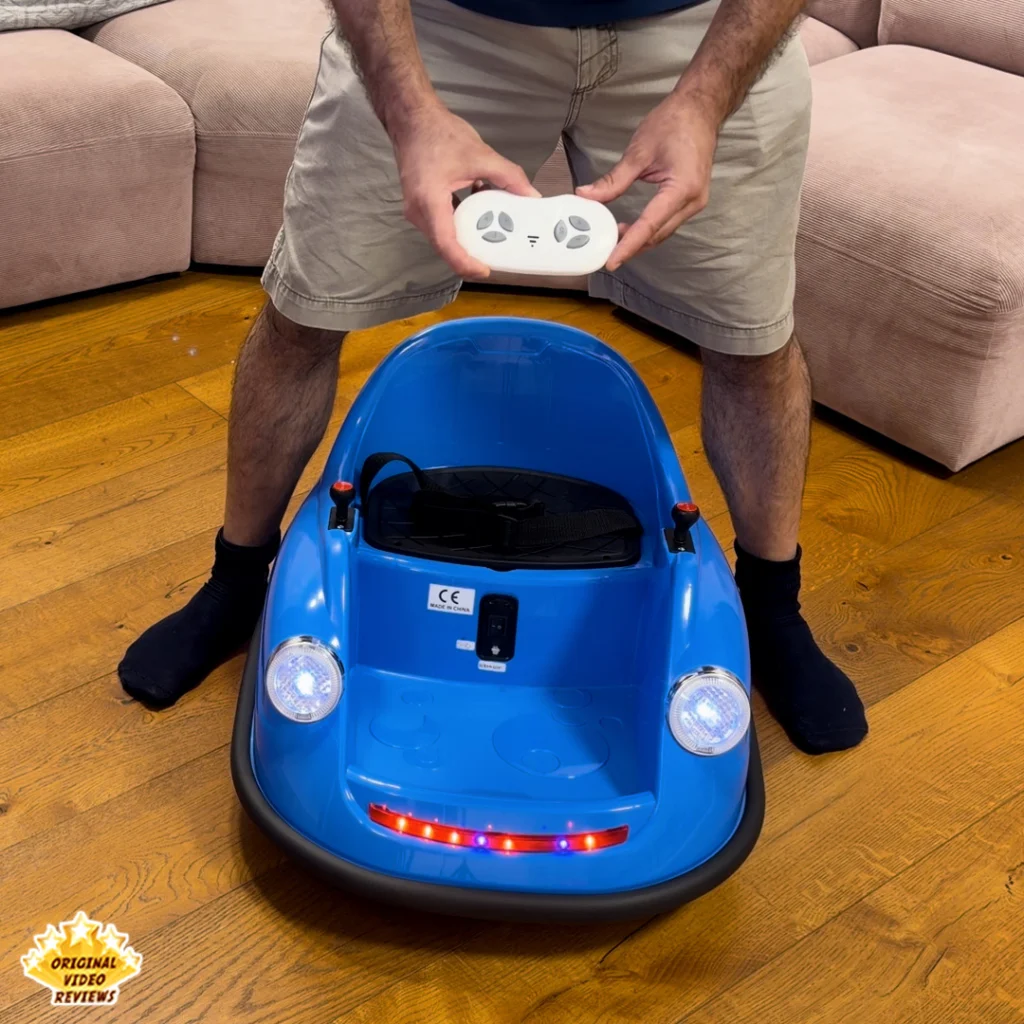 Person standing behind the Electric Bumper Car for Kids holding the wireless remote control, with the car’s headlights and LED strip lit