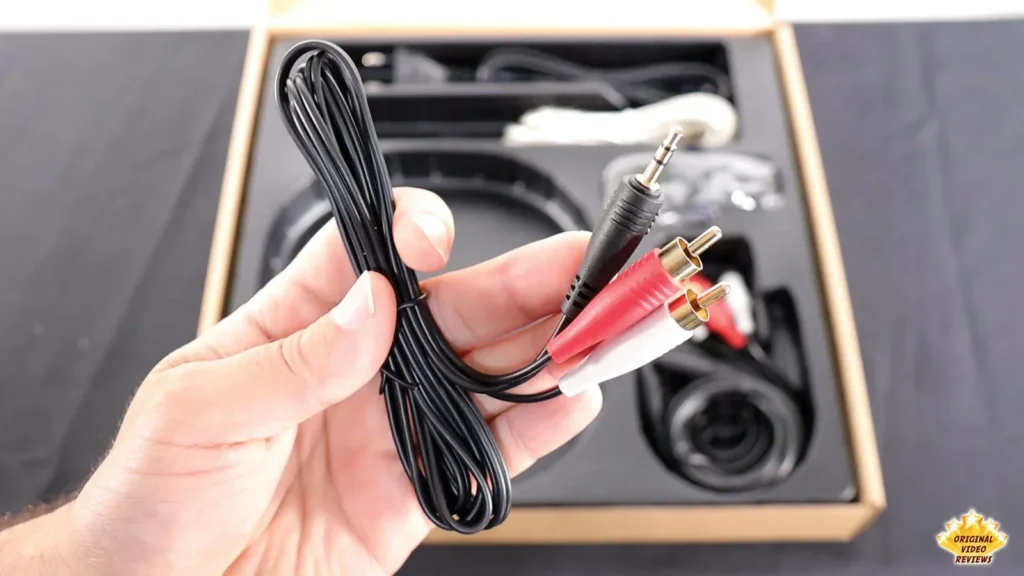 Hand holding a coiled 3.5mm-to-RCA audio cable from the AIRPULSE A100 box