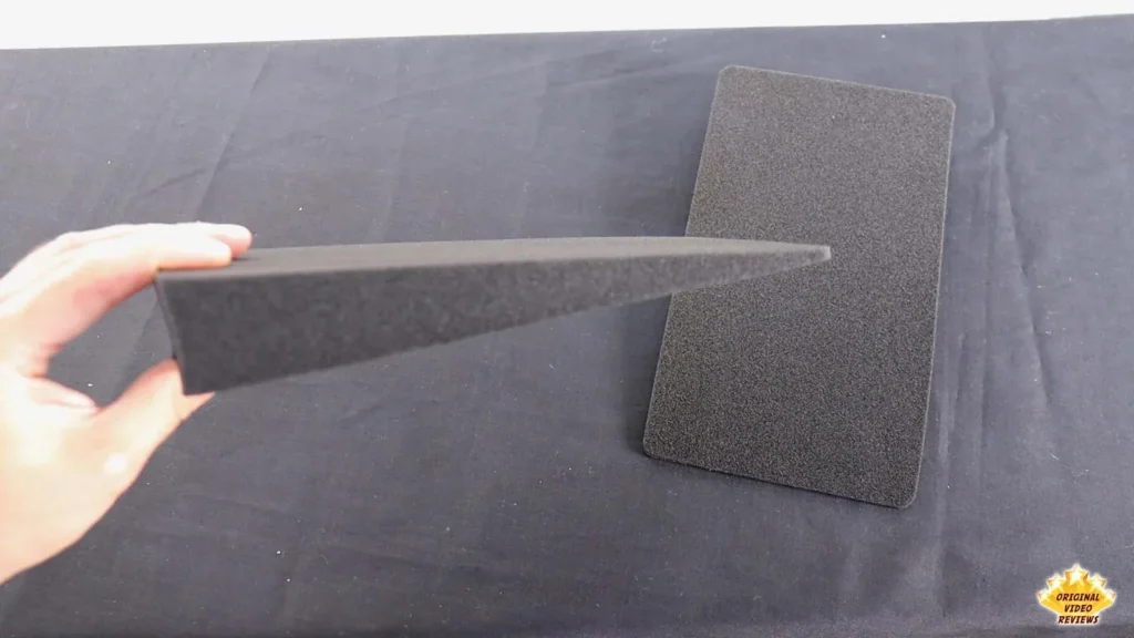 Hand holding an angled gray foam desk stand next to a flat foam pad