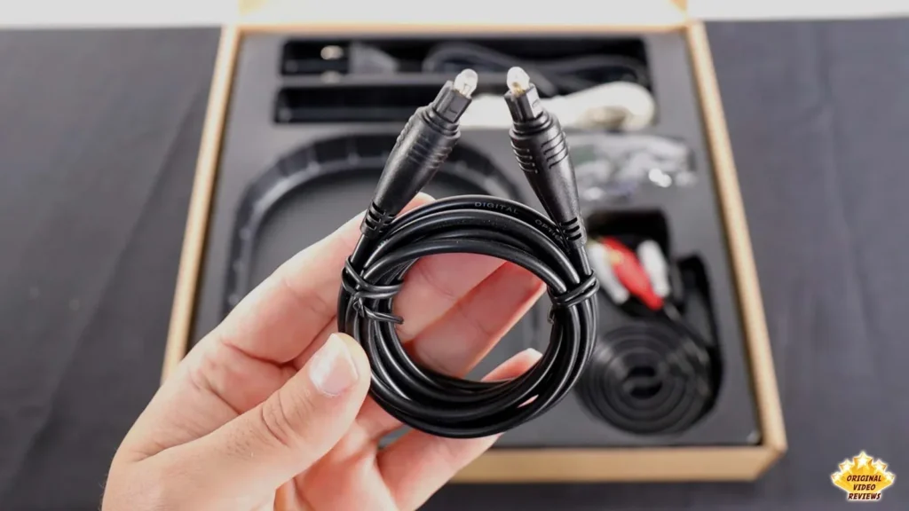 Hand holding a coiled black optical audio cable from the AIRPULSE A100 box