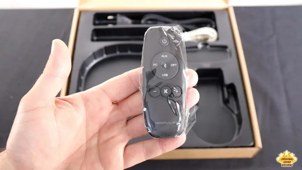 Hand holding the AIRPULSE A100 remote control still in its plastic bag