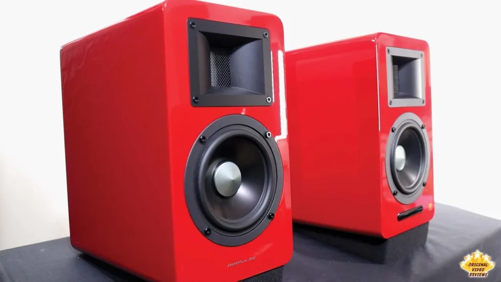 Close-up of a red AIRPULSE A100 speaker with its horn tweeter and woofer, next to the second speaker