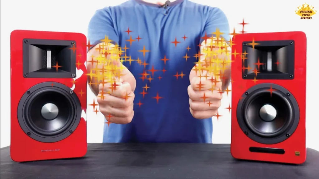 Reviewer (The OVR Guy) holding his hands out between two red AIRPULSE A100 speakers with a sparkle effect