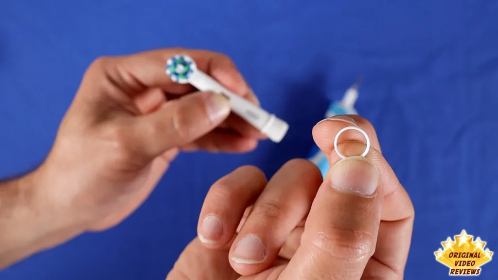 Hands holding an Oral-B brush head and a small ring on a blue surface