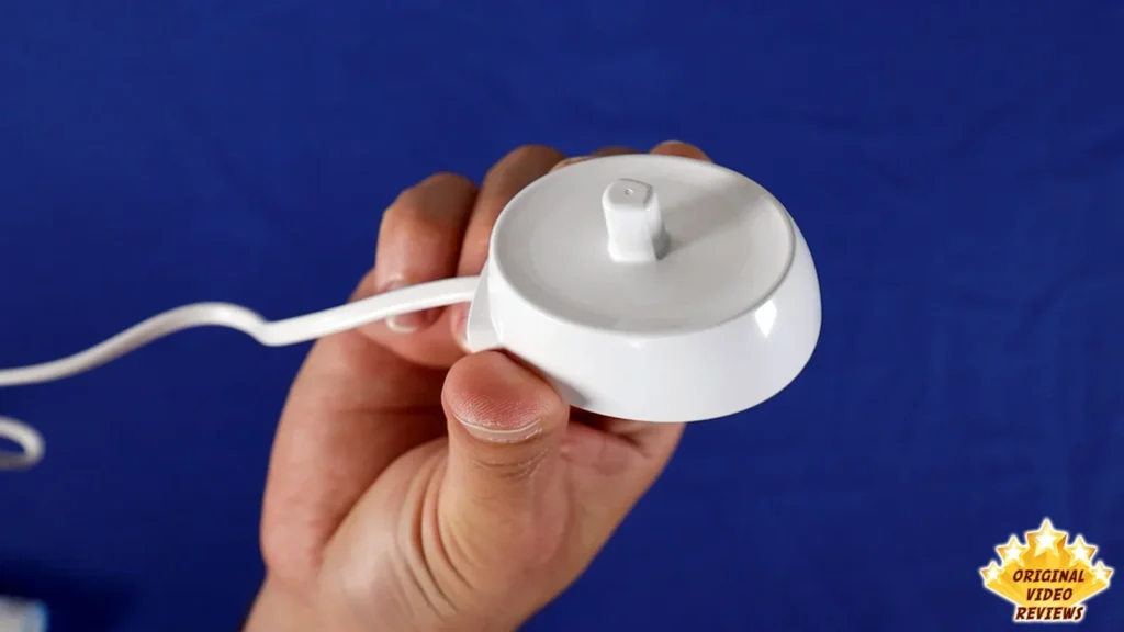 Hand holding the Oral-B Vitality charging unit with its cable on a blue surface