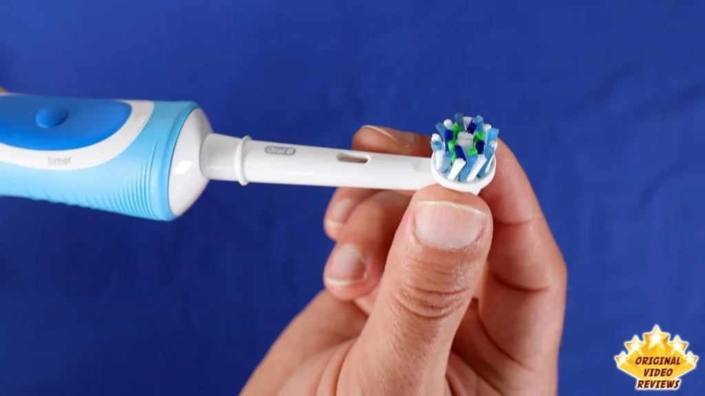 Hand holding an Oral-B CrossAction brush head in front of the Oral-B Vitality handle