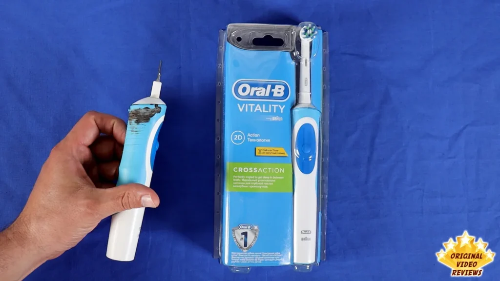 Hand holding the Oral-B Vitality toothbrush next to its retail box on a blue surface