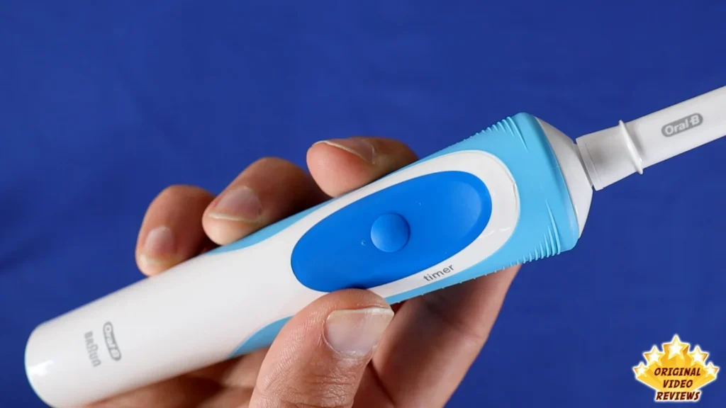 Hand holding the Oral-B Vitality handle, showing the power button, blue background