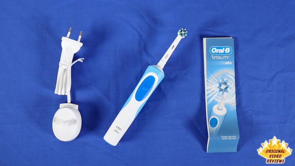 Oral-B Vitality electric toothbrush, charging unit with plug and retail box laid out on a blue surface